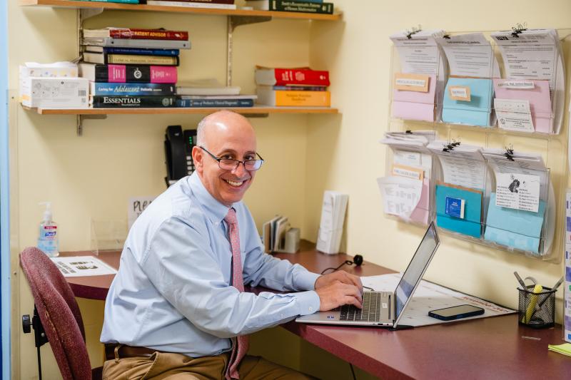 a man with a tie and glasses at a laptop smiling